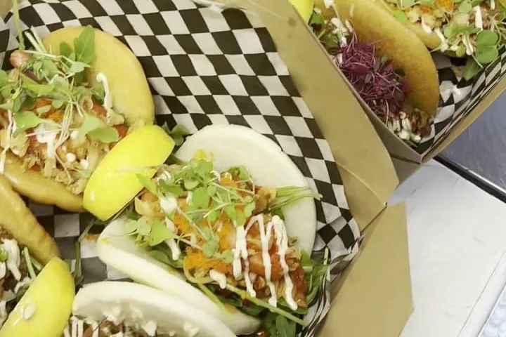 Shaka's bao buns with fresh greens and sauce, packed in checkered kraft takeout boxes.